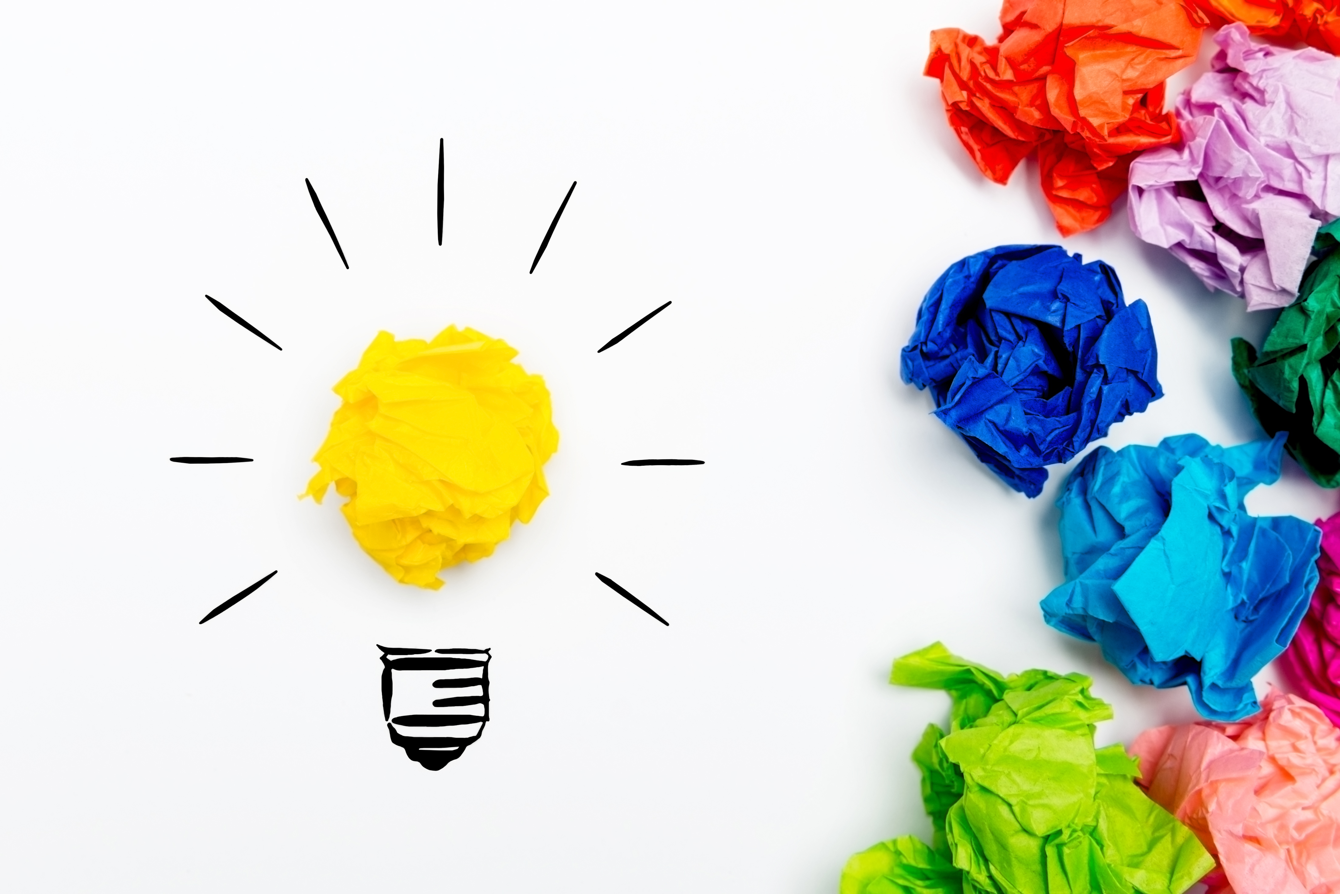Crumpled paper light bulb over white background, surrounded by crumpled colorful paper. Idea concept.